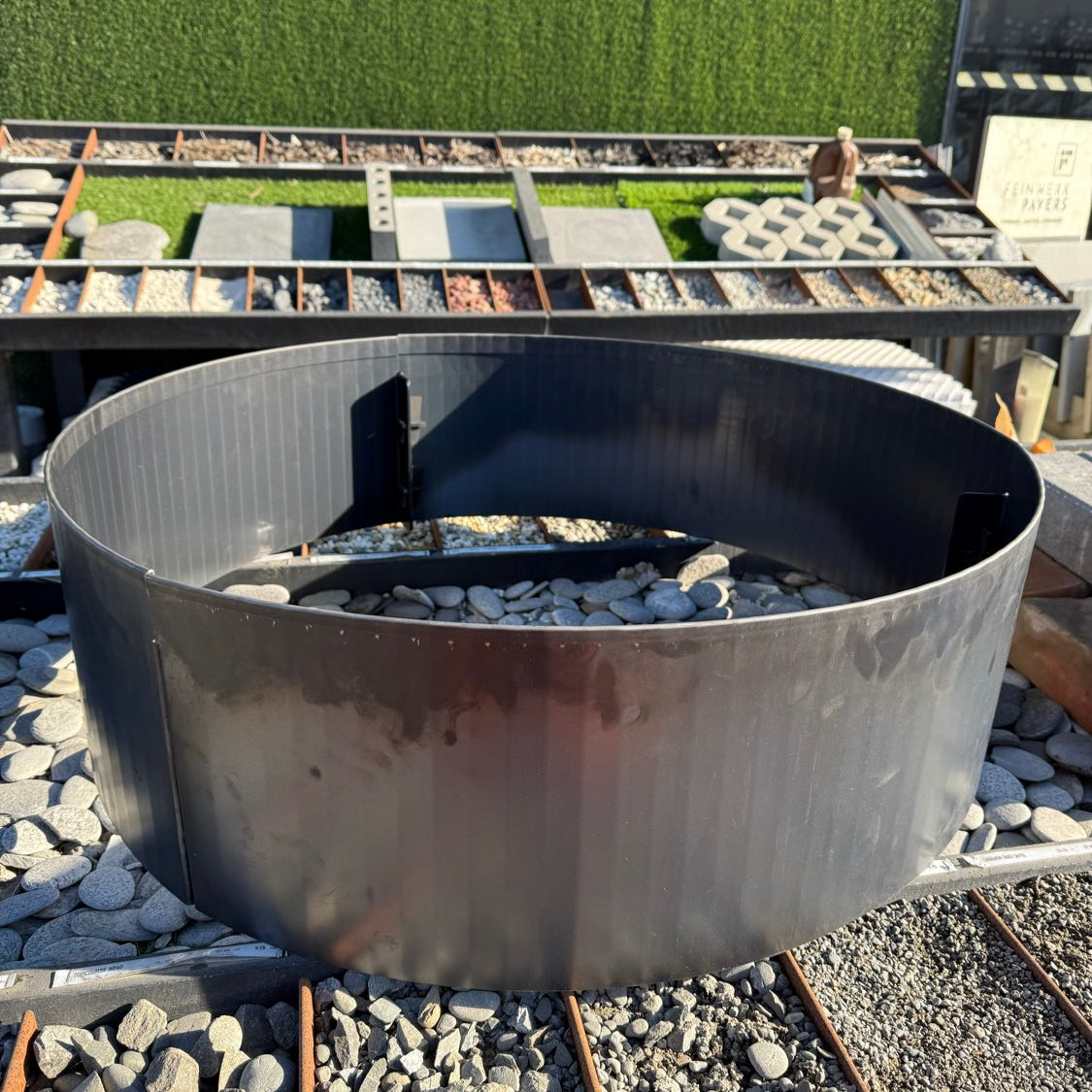 Metal fire pit on a gravel surface with a green grassy area in the background