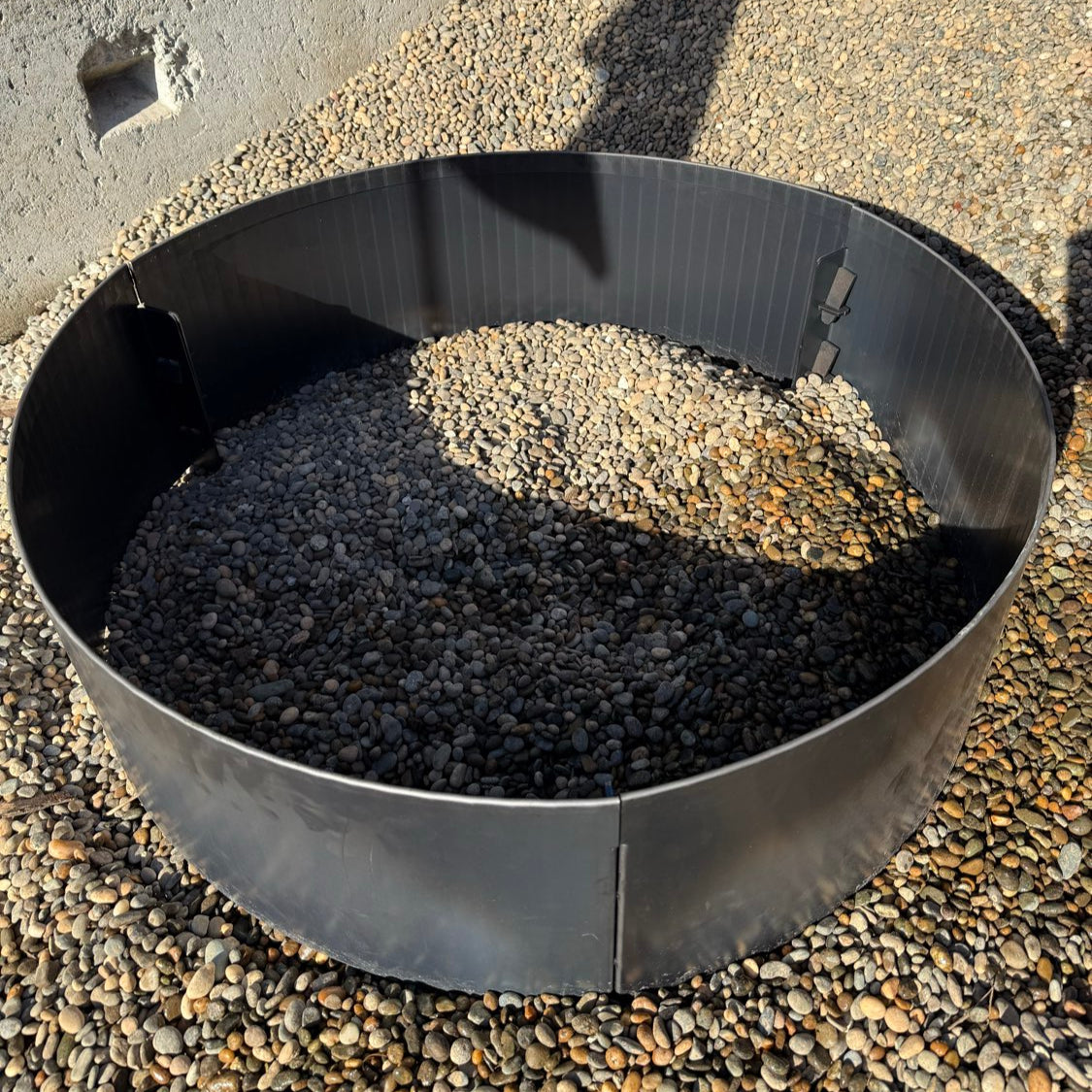 Black metal fire pit ring with stones on a gravel surface