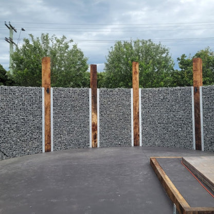 Gabion wall with wooden posts and trees in the background