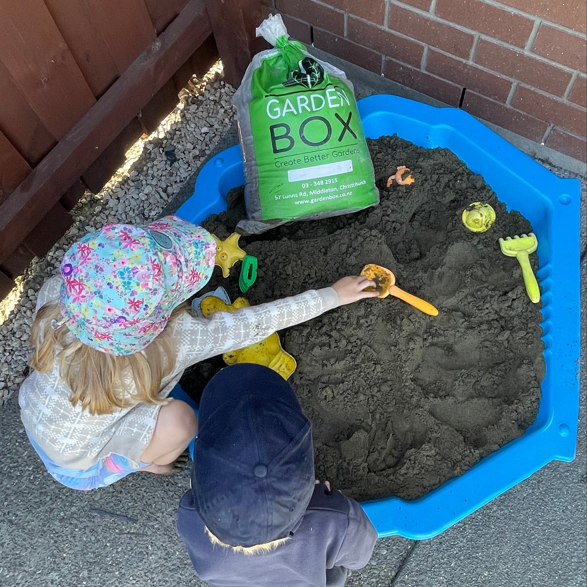 Two children playing with a Gardener's Box product in a sand pit.