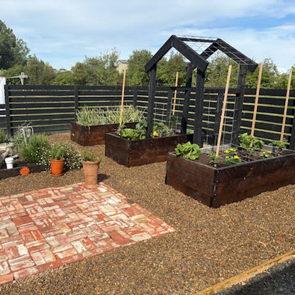Garden with raised beds and plants, featuring a brick patio area.